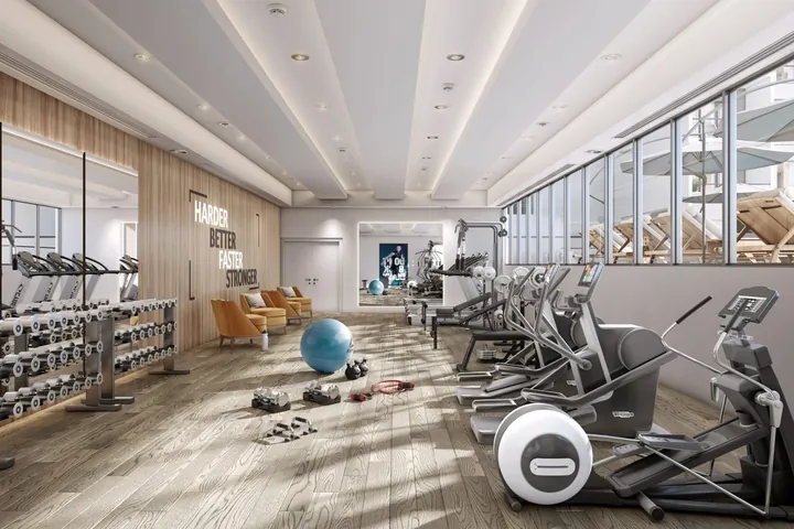 A gym with treadmills and cross-trainers beside tall windows